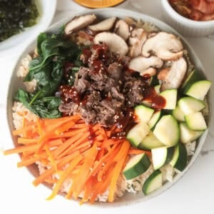 Overhead view of beef bibimbap with carrots, zucchini, mushrooms, and spinach.