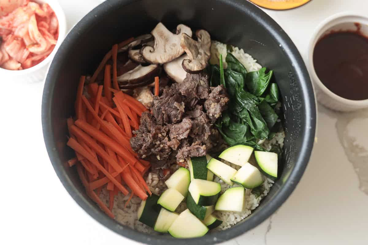 Top-down view of cooked beef and vegetable bibimbap in a rice cooker.